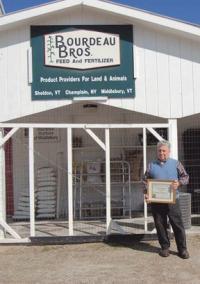 Jim Bushey holding his Business of the Month plaque in front of Bourdeau and Bushey, Inc. in Middlebury.