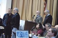 This year's Town Report was dedicated to the firefighters and police who worked to save downtown Middlebury from catastrophic consequences when gasoline-filled railroad tankers derailed and one began leaking last October. Here Select Board chairman John Tenny (left, podium) and board member Dean George honor Fire Chief Rick Cole (left, on left) and Police Chief Thomas Hanley at Town Meeting. Municipal planner Fred Dunnington is in the foreground, at the computer.