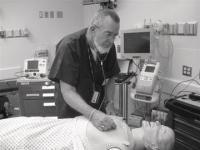 Dennis Maloney listening to the heart beat of one of the four mannequins in the Operating Room at the Clinical Simulation Lab.