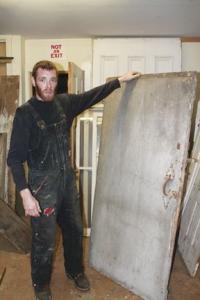 Artist and furniture maker Adam Marsano stands beside a piece of  King’s Pine that once stood in the original Vermont canopy in the 1750’s and first served as doors in the Brandon Town Hall. A part of living Vermont history, including even possibly having witnessed Ethan Allen, this reclaimed lumber will again be a vibrant part of a home, business or part of an original piece of furniture. 